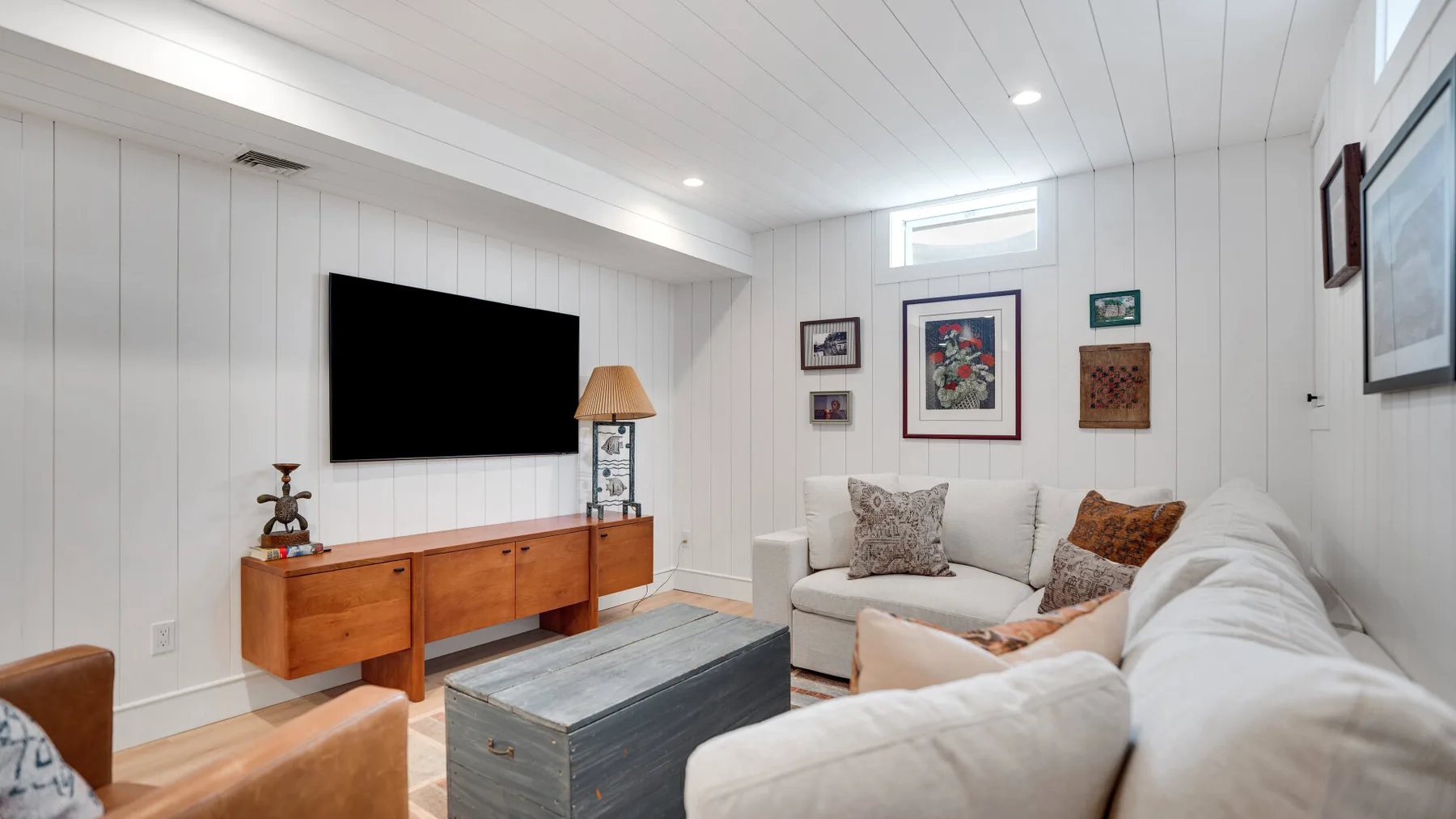 Una sala luminosa con televisor, consola de madera y asientos de tonos claros.