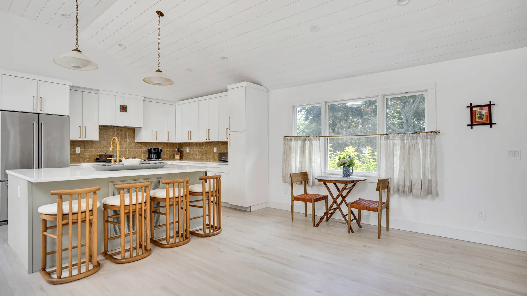 Una luminosa cocina y comedor con una isla central y una mesa junto a la ventana.