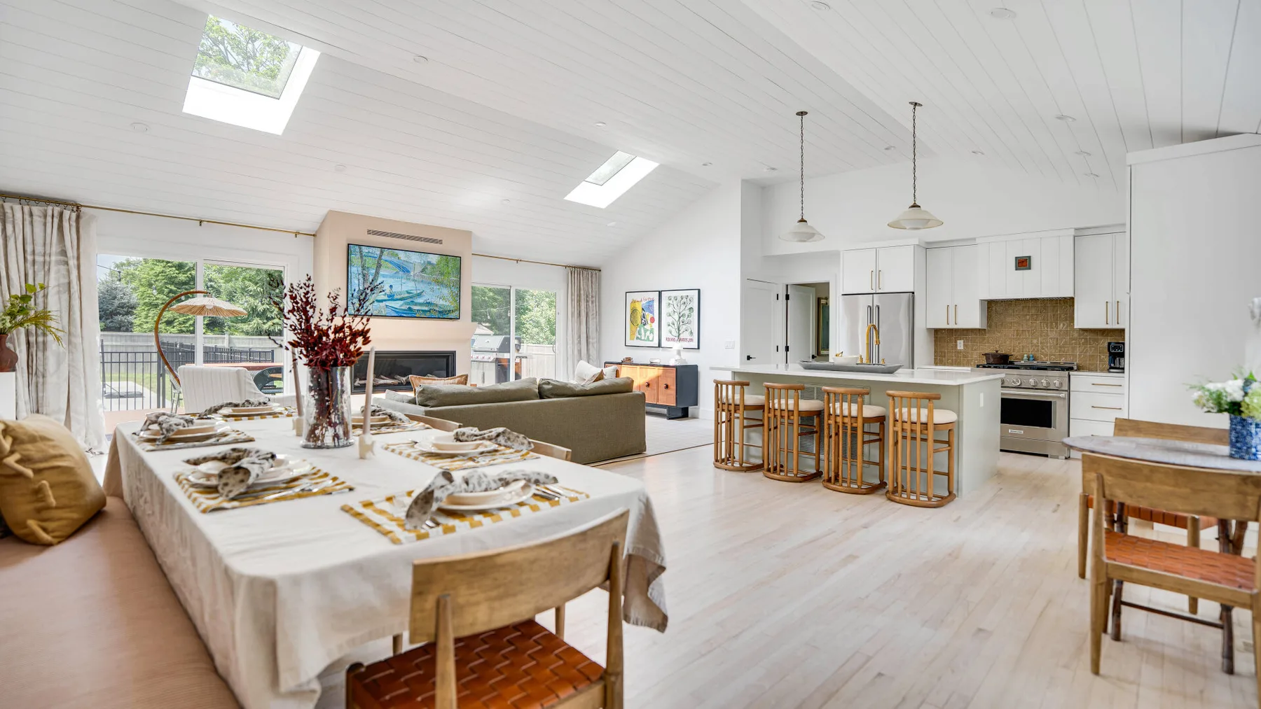 Espacio abierto de comedor y cocina, con una mesa larga preparada y asientos junto a la isla.