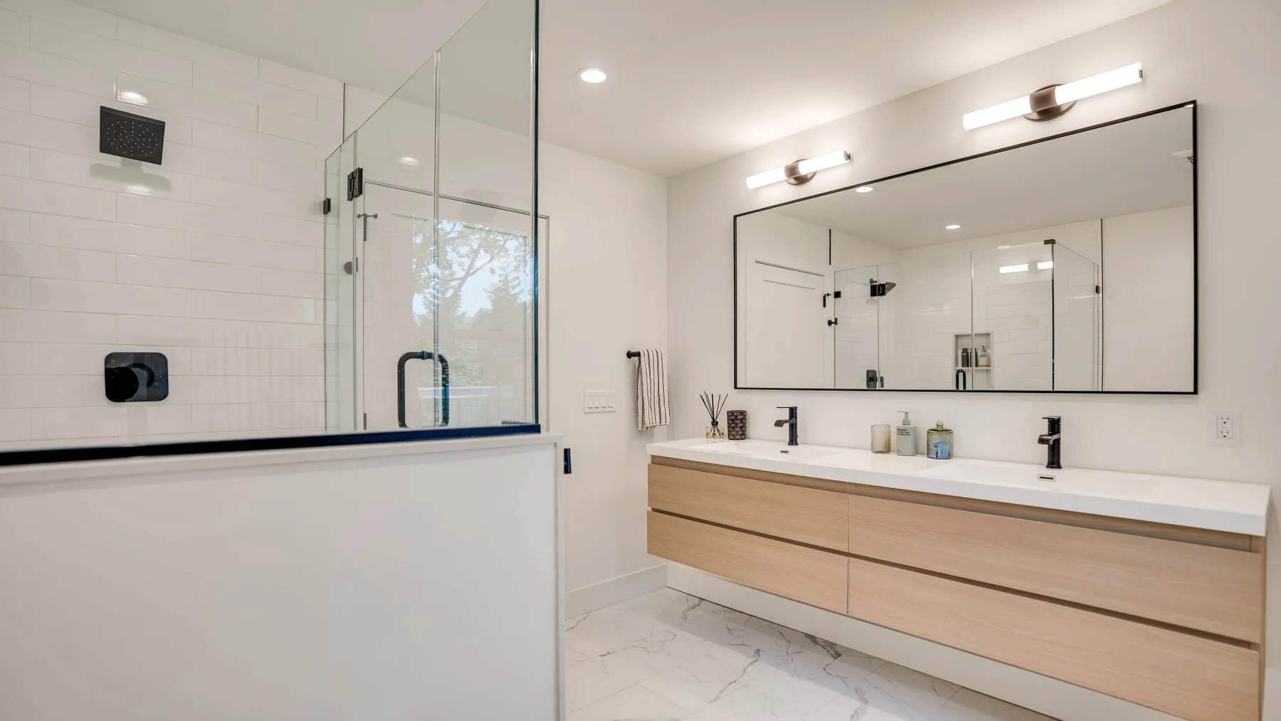Un baño luminoso con una ducha de vidrio y un amplio lavabo bajo un espejo grande.