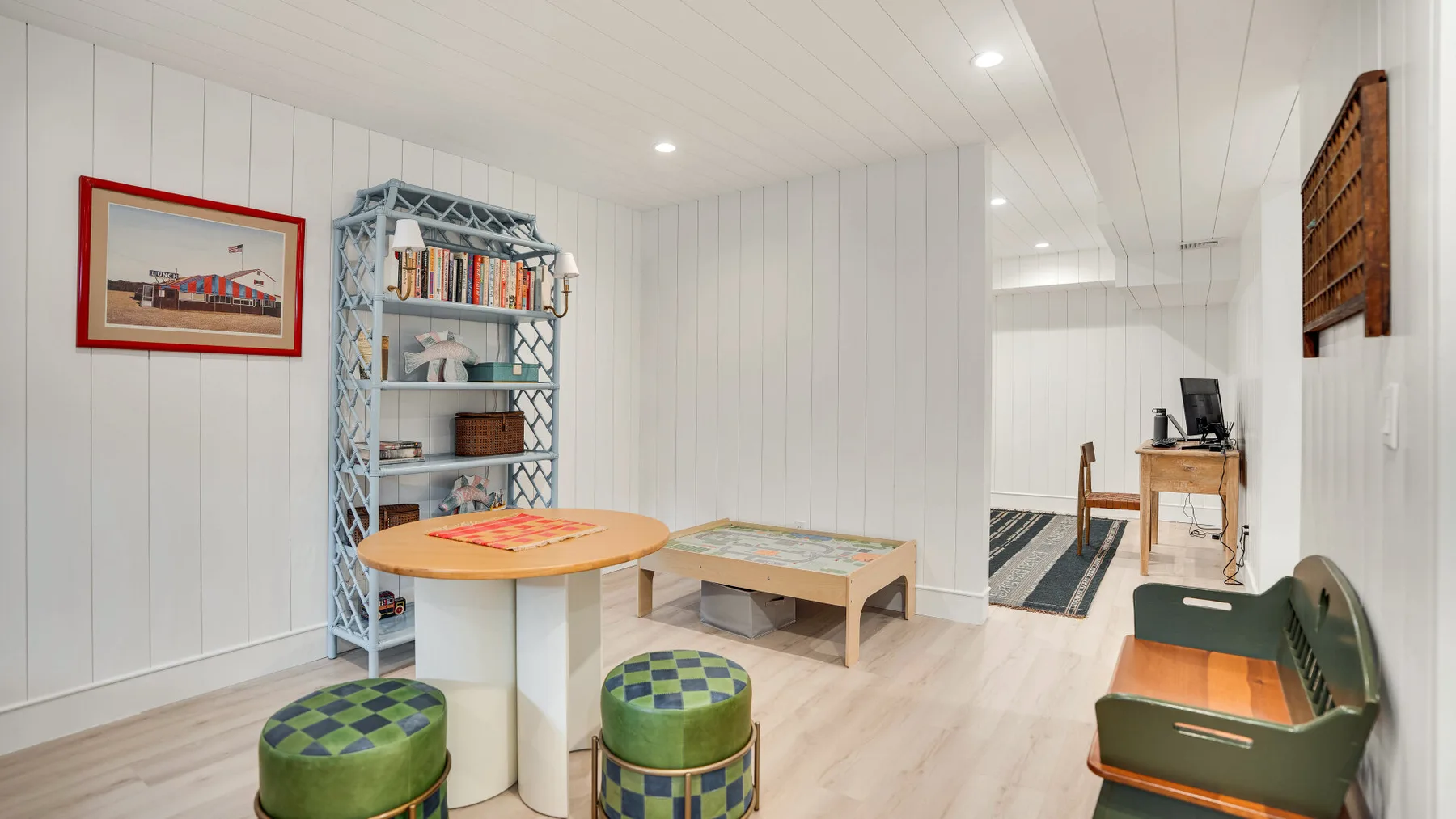 Una luminosa sala de estar en el sótano con mesa, taburetes, estantería y escritorio.