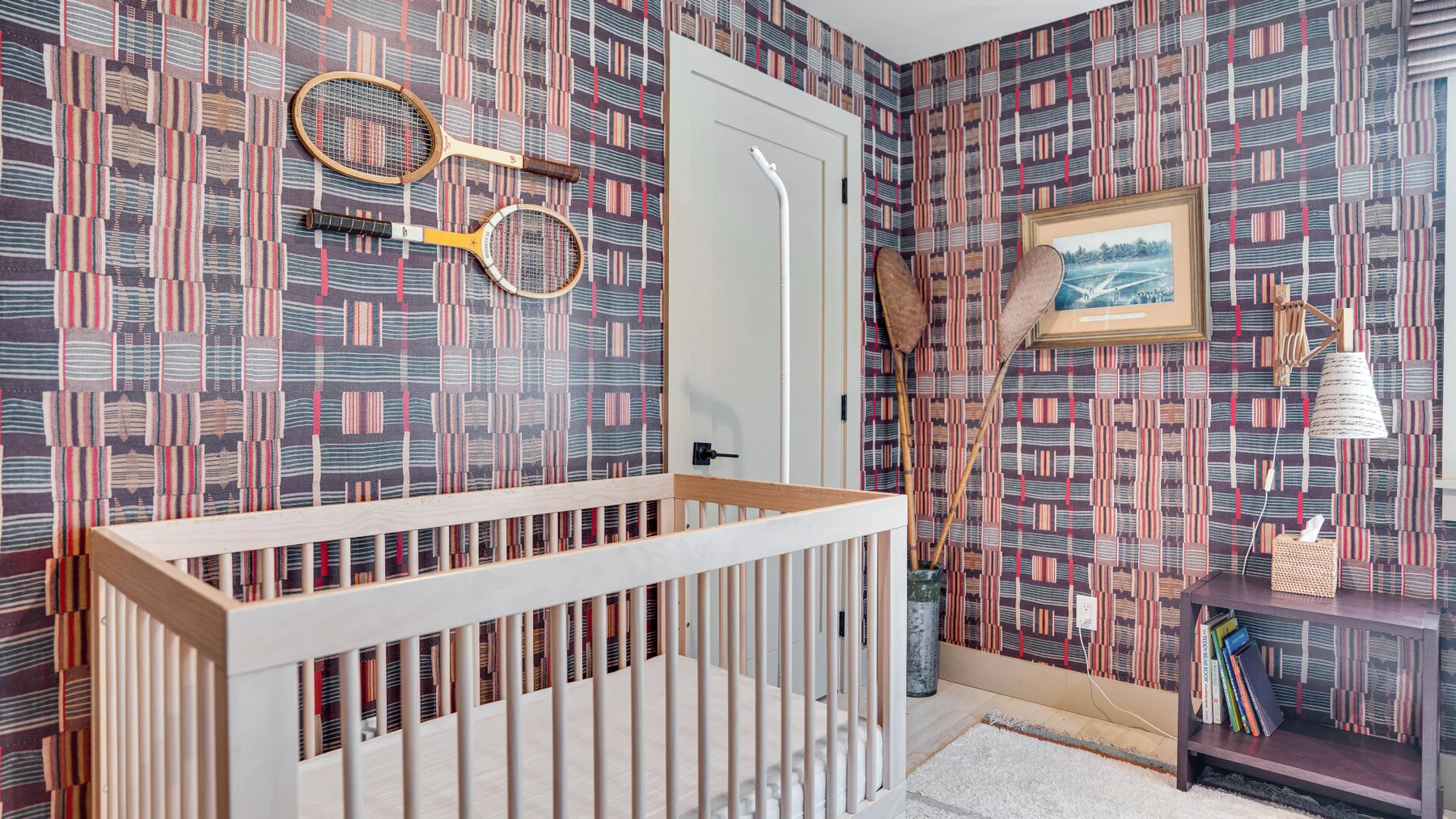 Un cuarto infantil con una cuna de madera, papel tapiz estampado y una pequeña estantería.
