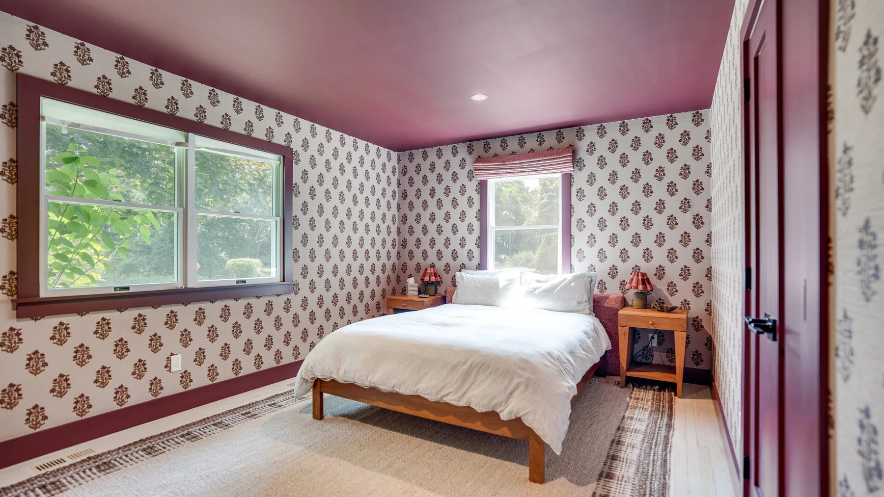 Un dormitorio con una cama, papel tapiz estampado y ventanas con vista a la vegetación.