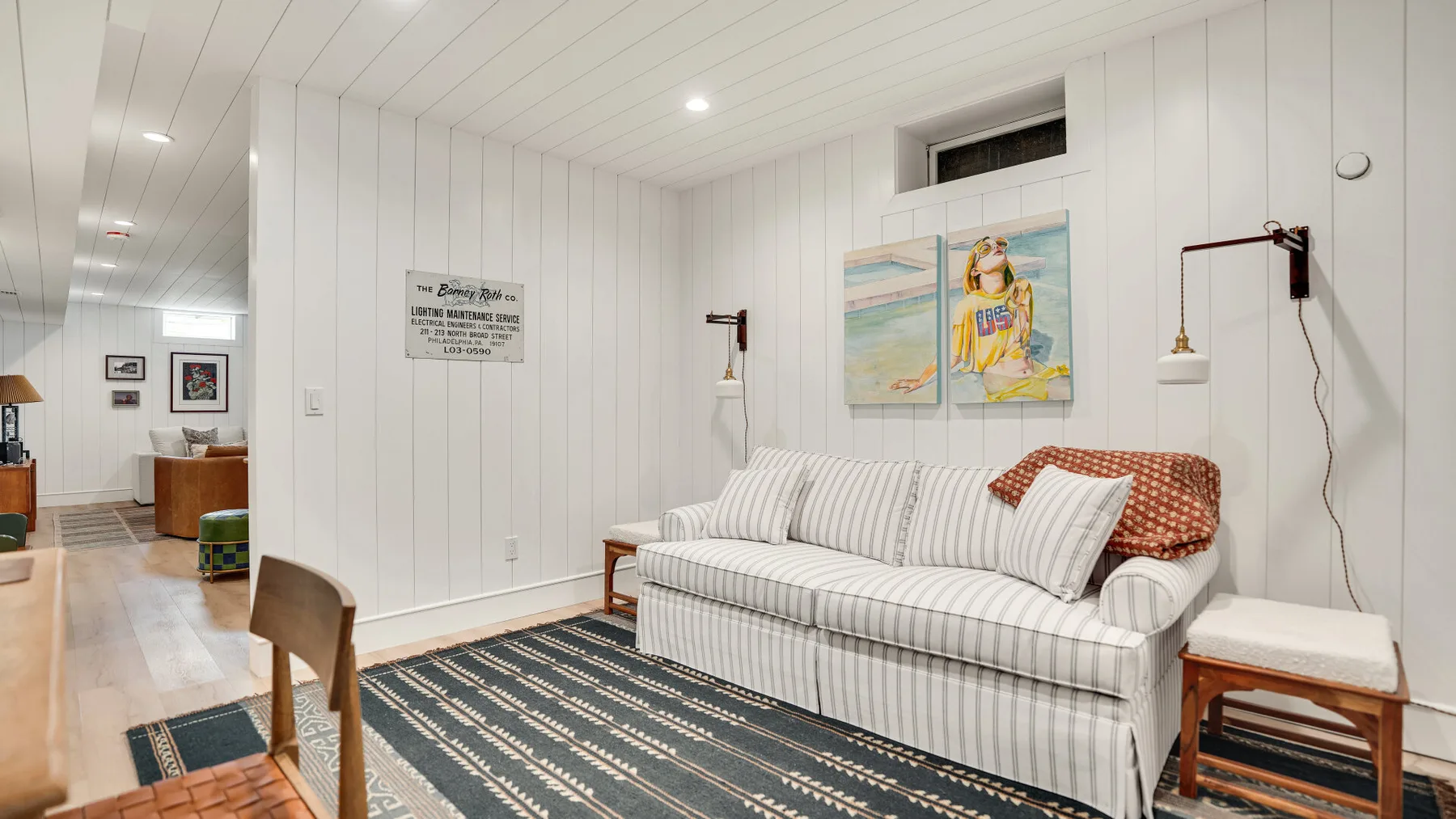 Un dormitorio luminoso con una cama a rayas y obras de arte coloridas en la pared.