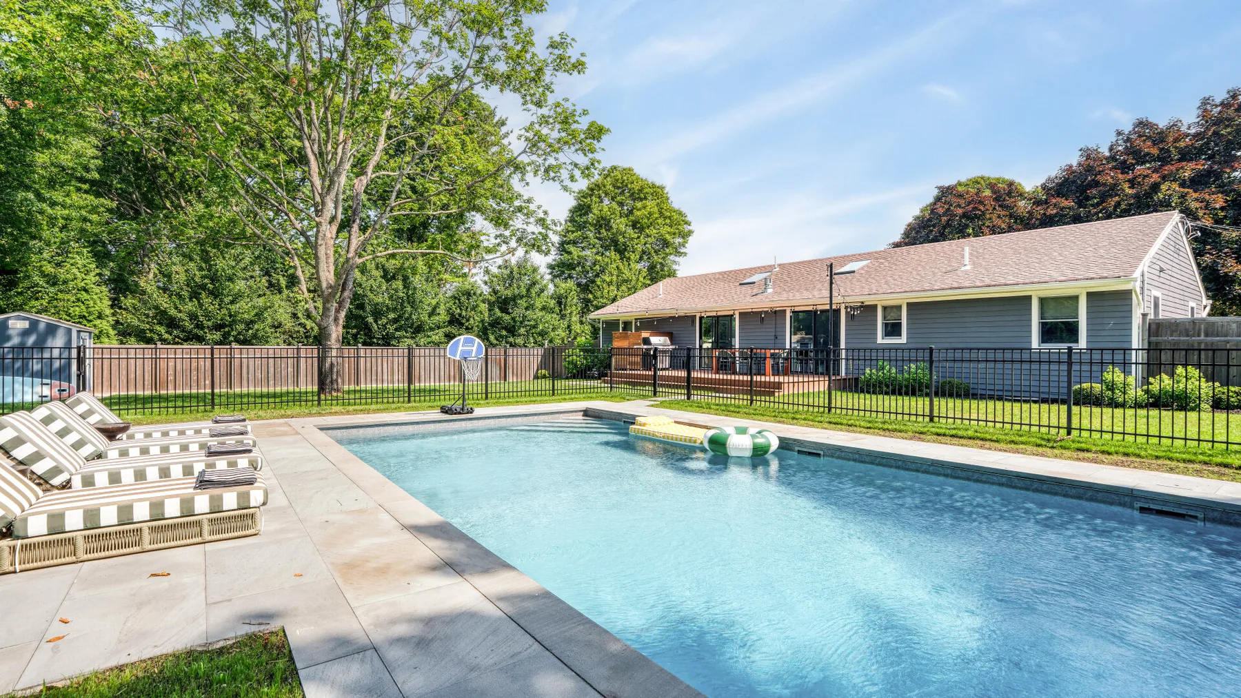 Piscina exterior junto a una terraza pavimentada, asientos y un edificio cercado.