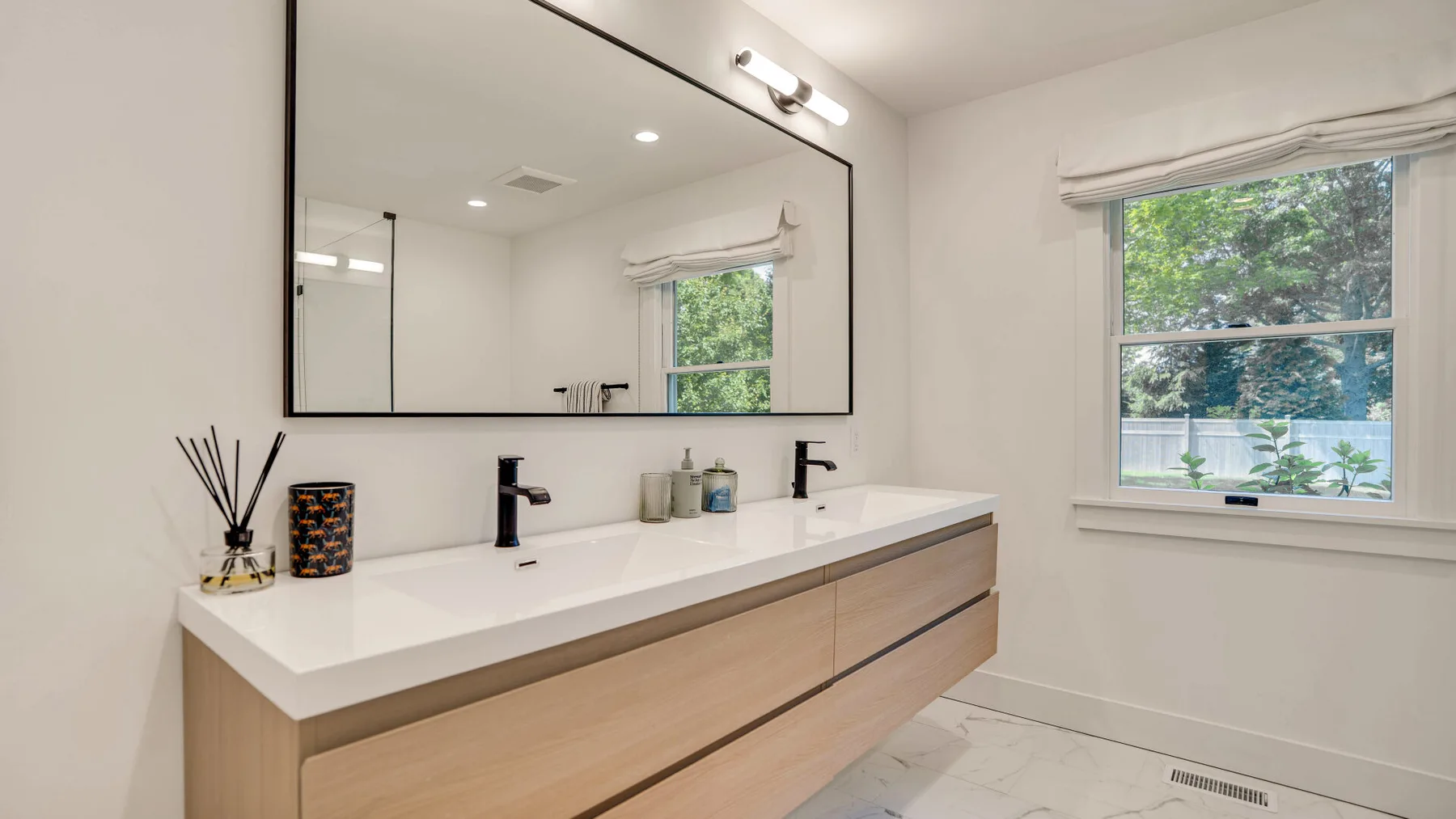 Un baño luminoso con un mueble largo, dos lavabos y un espejo grande.