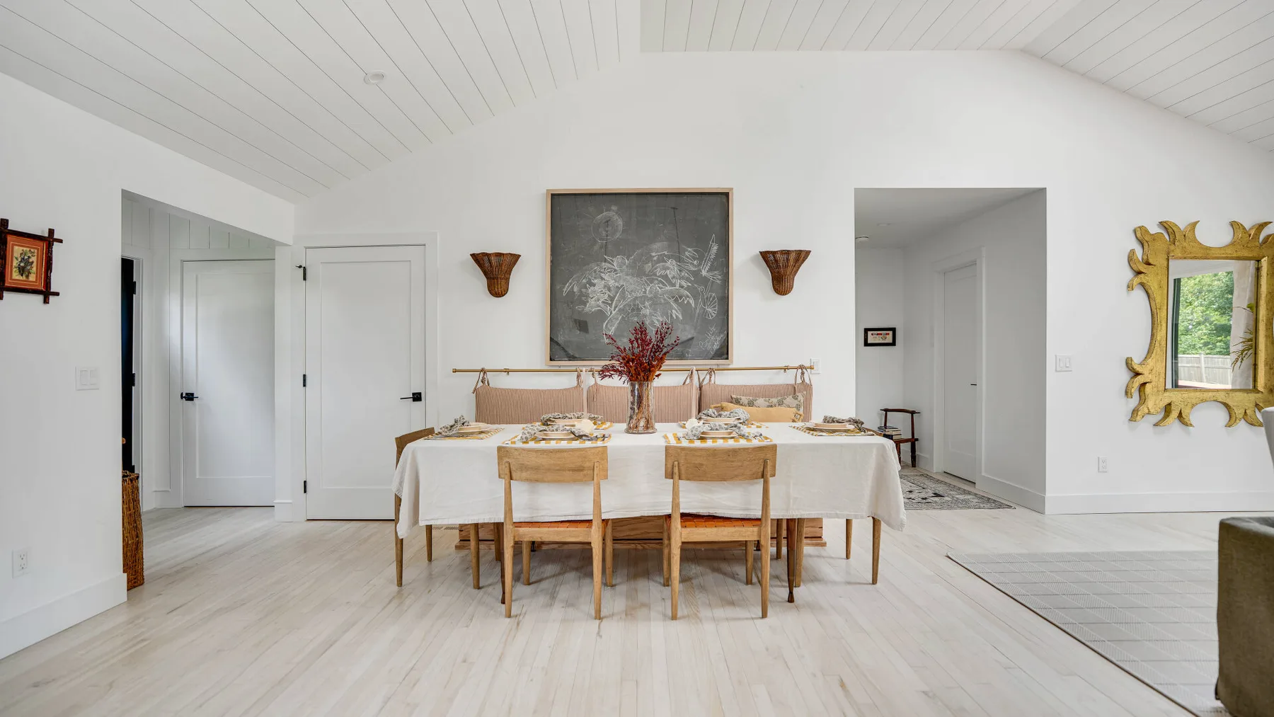 Un comedor luminoso con una mesa larga puesta bajo un cuadro enmarcado.