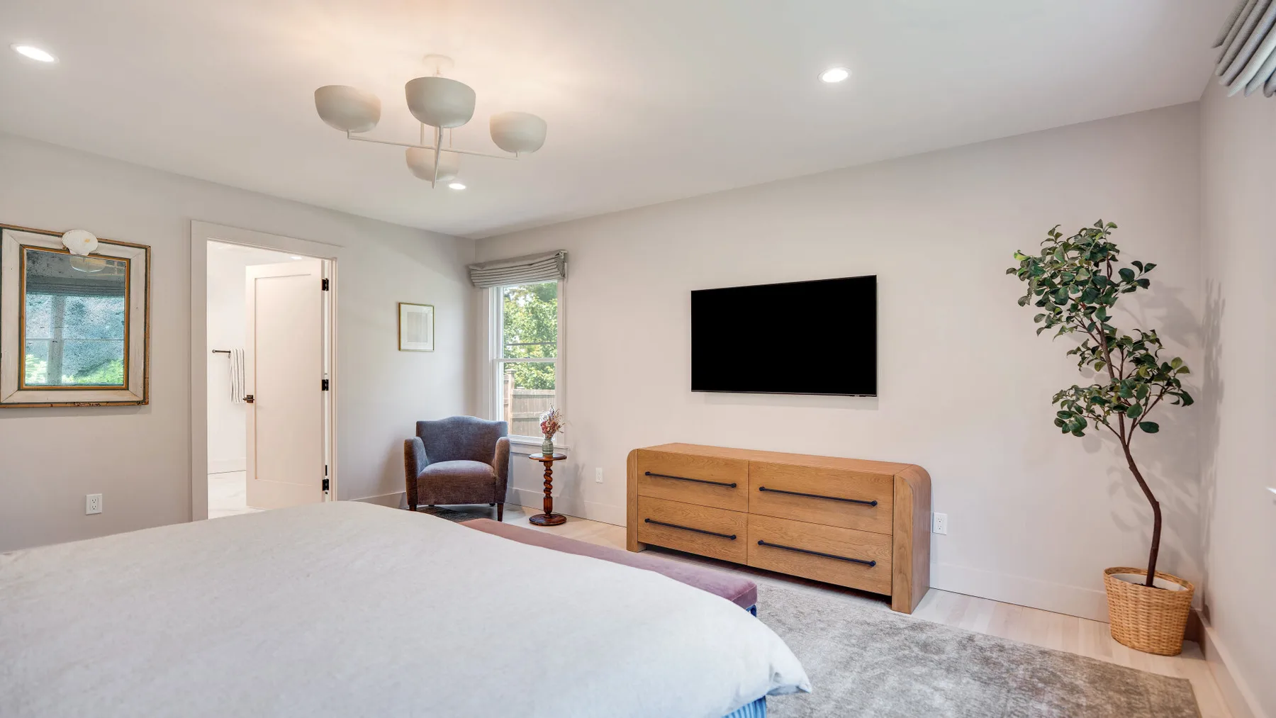 Un dormitorio luminoso con una cama, un televisor y una cómoda de madera.
