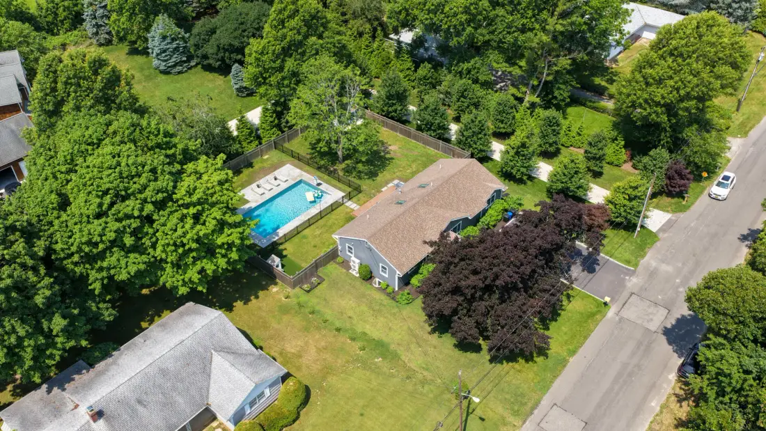 Vista aérea de una casa, una piscina y patios arbolados alrededor.