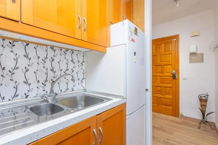 A compact kitchen with orange cabinets, a sink, and a refrigerator beside a wooden door.
