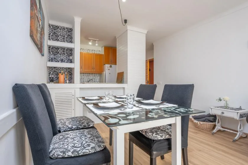 A dining area with a glass-top table and patterned seating beside an open kitchen.