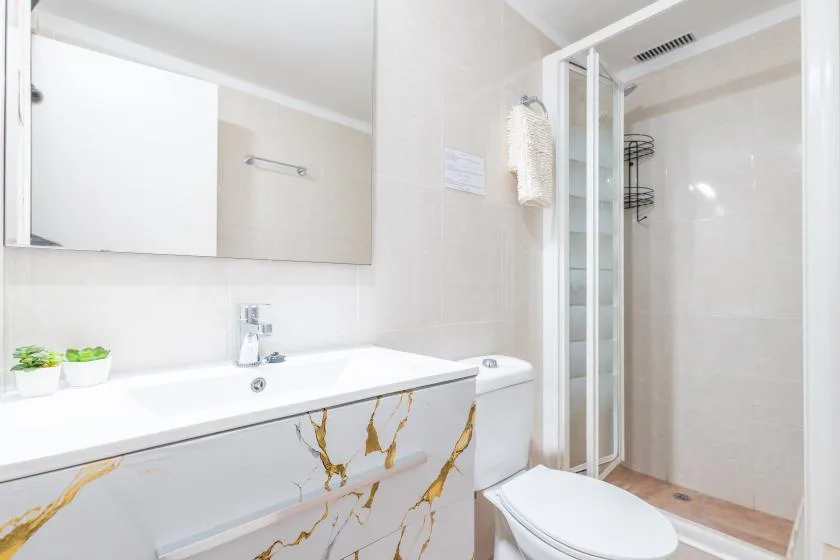 A bright bathroom with a sink, mirror, toilet, and shower.