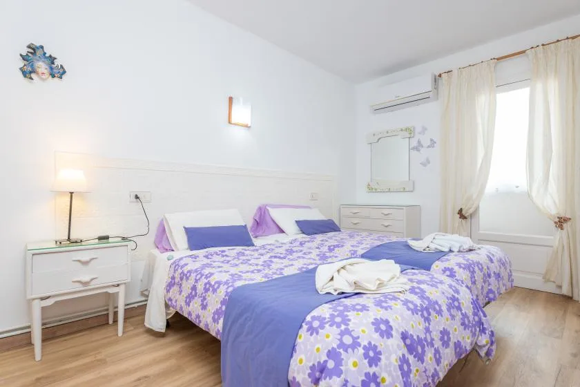 A bright bedroom with two beds dressed in purple floral bedding.