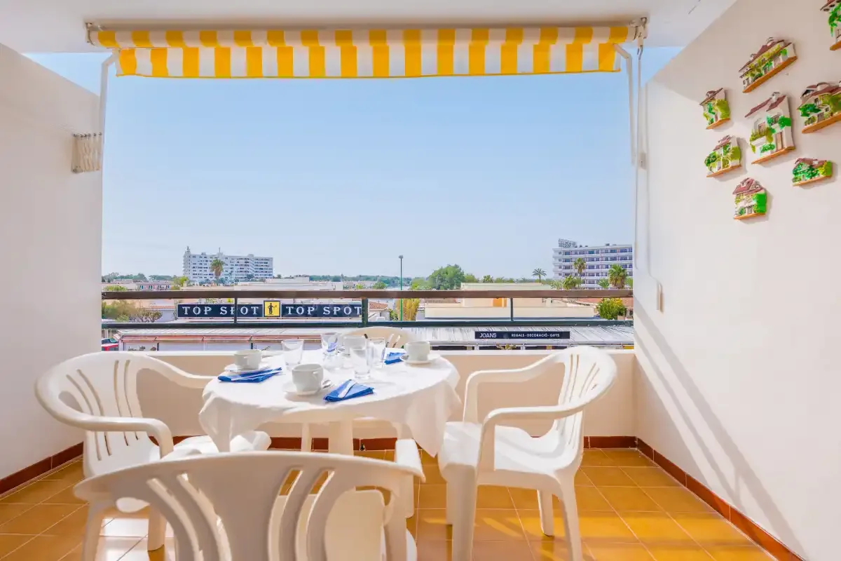 A balcony dining area with a table and white seating overlooking the outdoors.