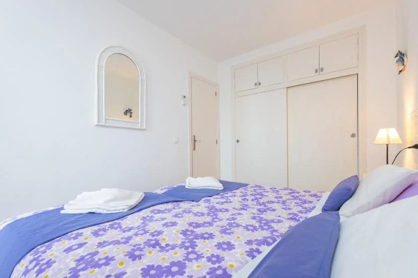 A bedroom with a floral bedspread, folded towels, and built-in cupboards.