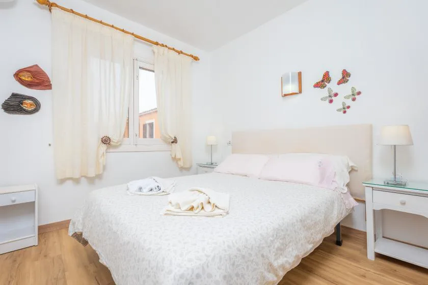 A bright bedroom with a double bed, white bedding, and sheer curtains.