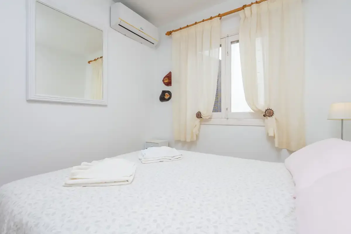 A bright bedroom with a bed and a curtained window.