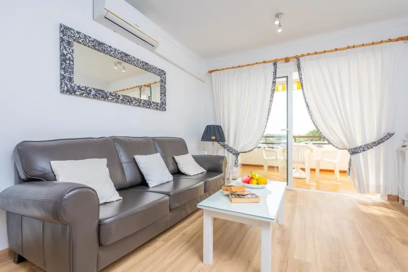 A bright living room with a sofa, coffee table, and curtains opening onto a balcony.