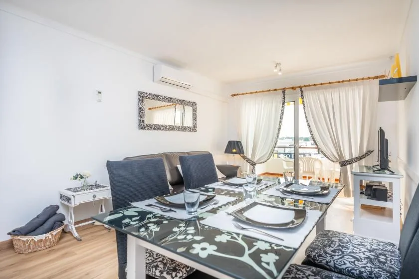 Dining area with a set table beside curtained windows opening onto a balcony.