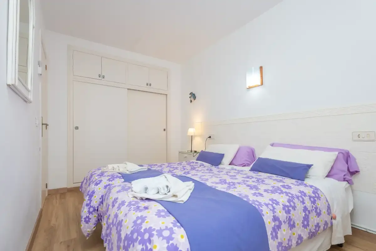 A bedroom with a double bed covered in purple floral bedding.