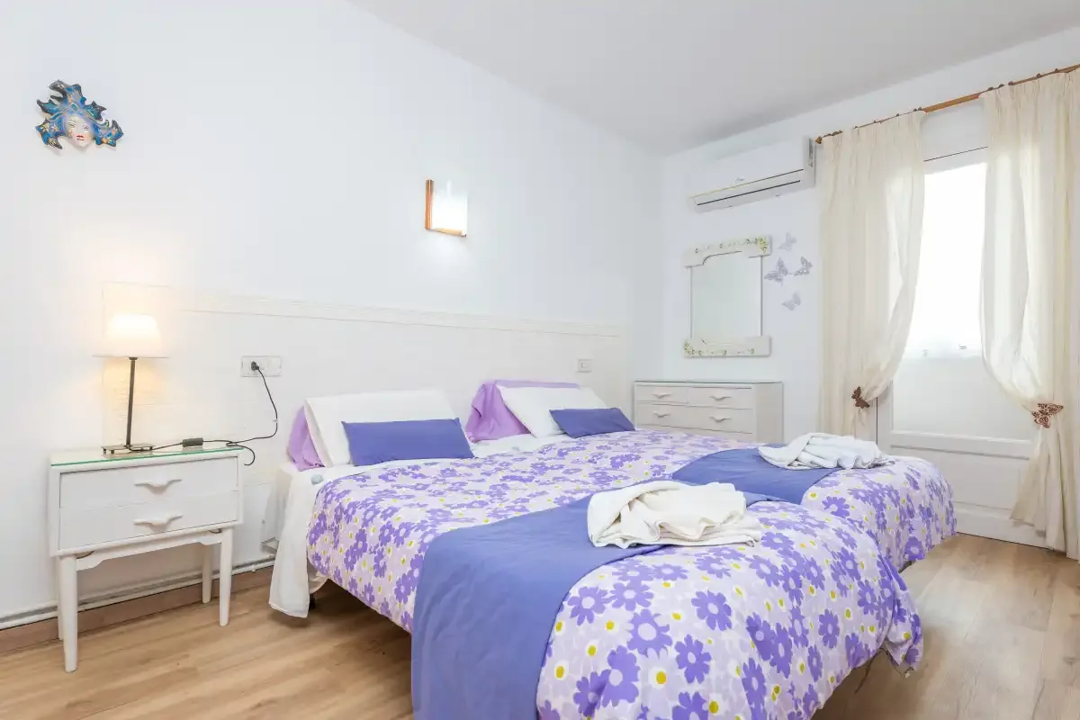 A bright bedroom with two beds dressed in purple floral bedding.