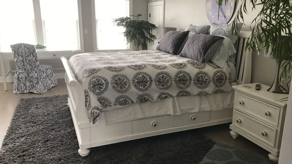 Un dormitorio luminoso con una cama estampada y una cómoda de noche.