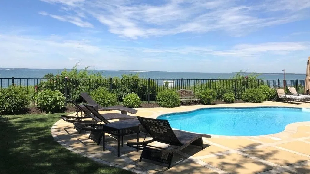 An outdoor swimming pool with lounge seating overlooks the ocean.