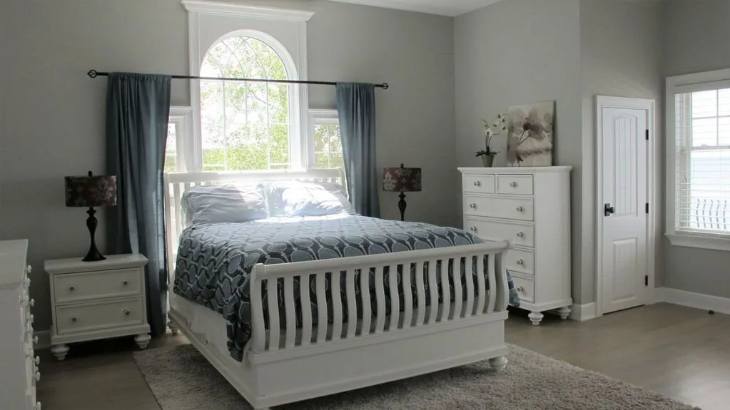 Un dormitorio con una cama bajo una ventana arqueada y una cómoda blanca.