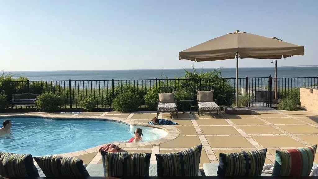 A swimming pool beside a patio with seating and an ocean view.