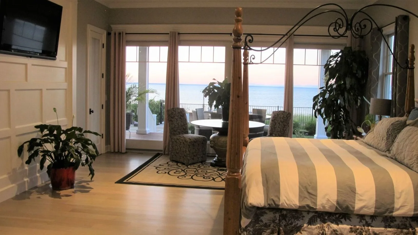 Un dormitorio con una cama a rayas, asientos y puertas de vidrio con vista al agua.