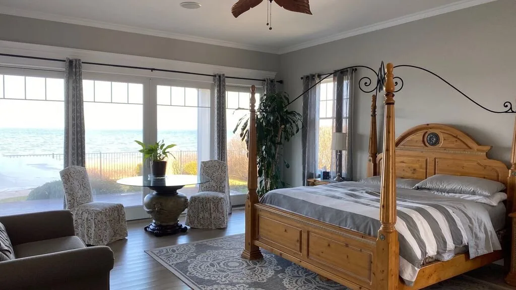 Un dormitorio con una cama de madera con dosel y grandes ventanas con vistas al agua.