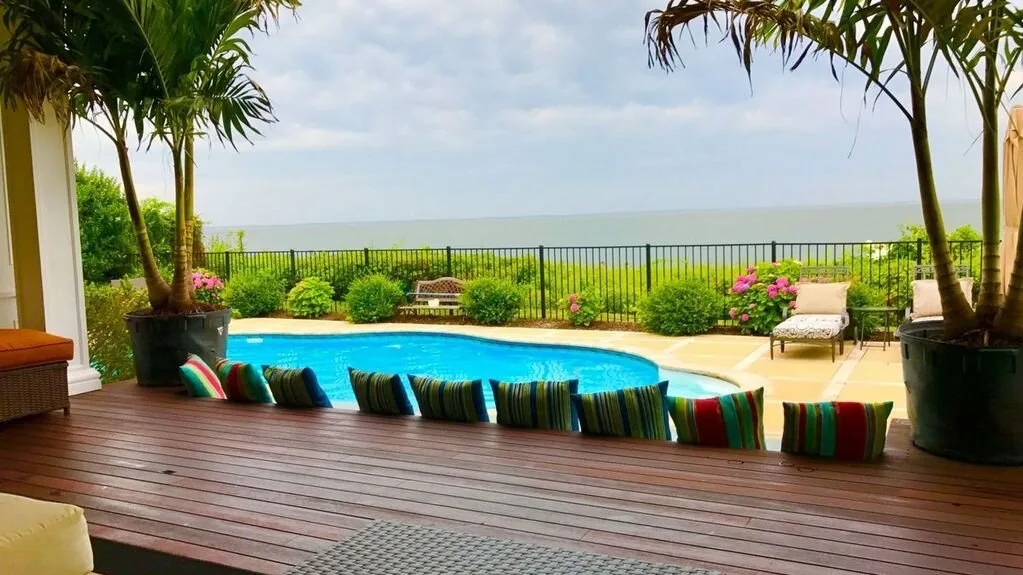 A poolside patio overlooks a green landscape, with cushioned seating along the pool.