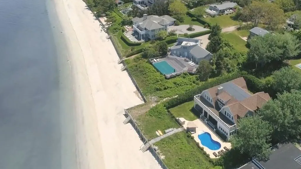 Vista aérea de casas junto a la playa, con una piscina al lado de la orilla arenosa.