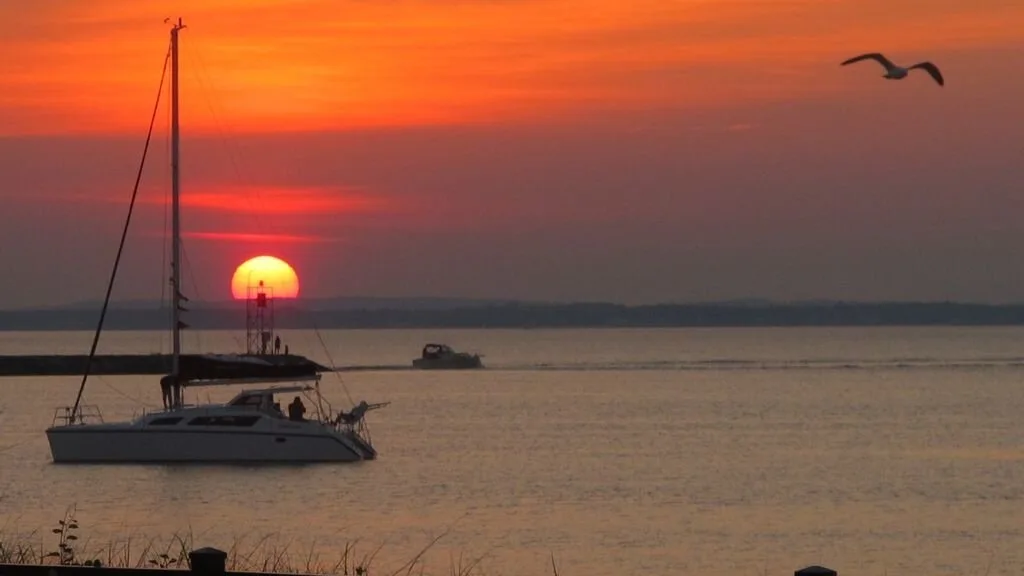 Un velero flota sobre aguas tranquilas bajo un intenso atardecer naranja.
