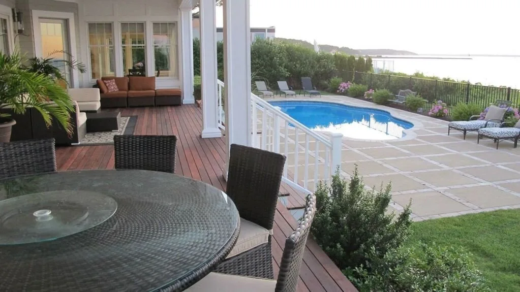 Un patio cubierto con una mesa redonda da a una piscina y una zona de asientos.