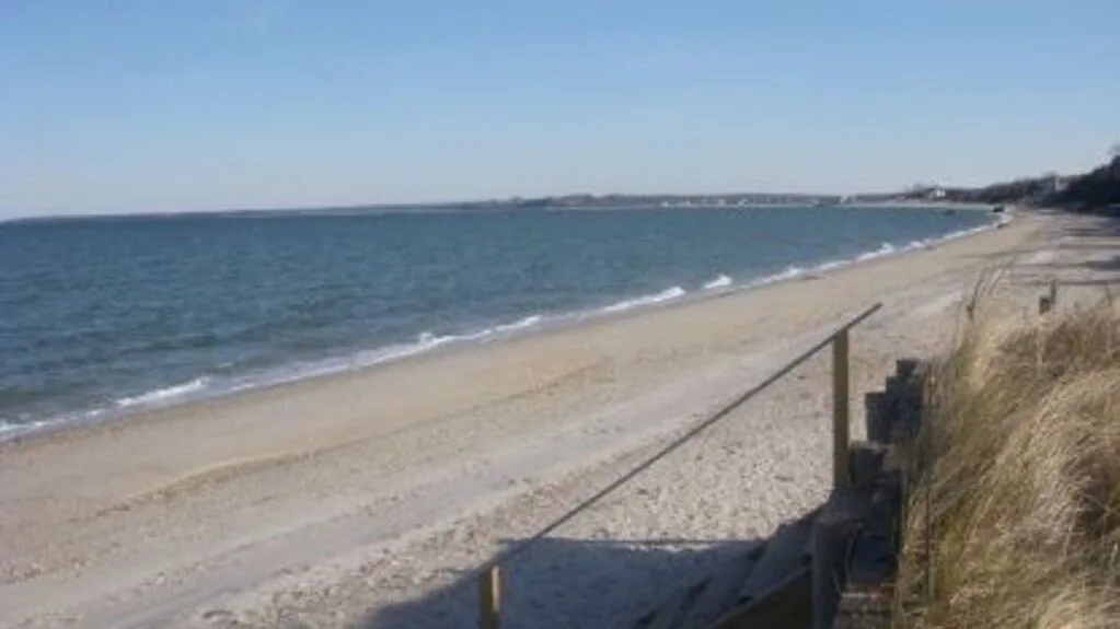 Una playa de arena se extiende junto a la costa y una duna cubierta de hierba.
