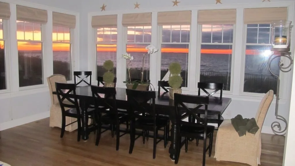 Comedor con asientos oscuros alrededor de una mesa junto a ventanas con vistas al atardecer.
