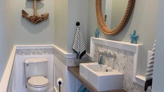 Un baño con inodoro, lavabo blanco y un espejo ovalado grande.
