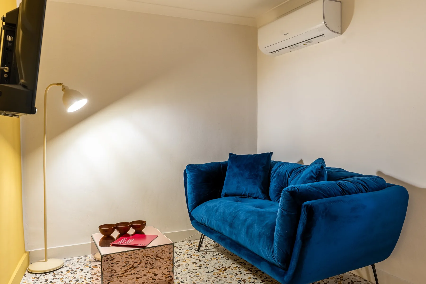 Una sala de estar con asientos azules, una lámpara de pie y una mesita.