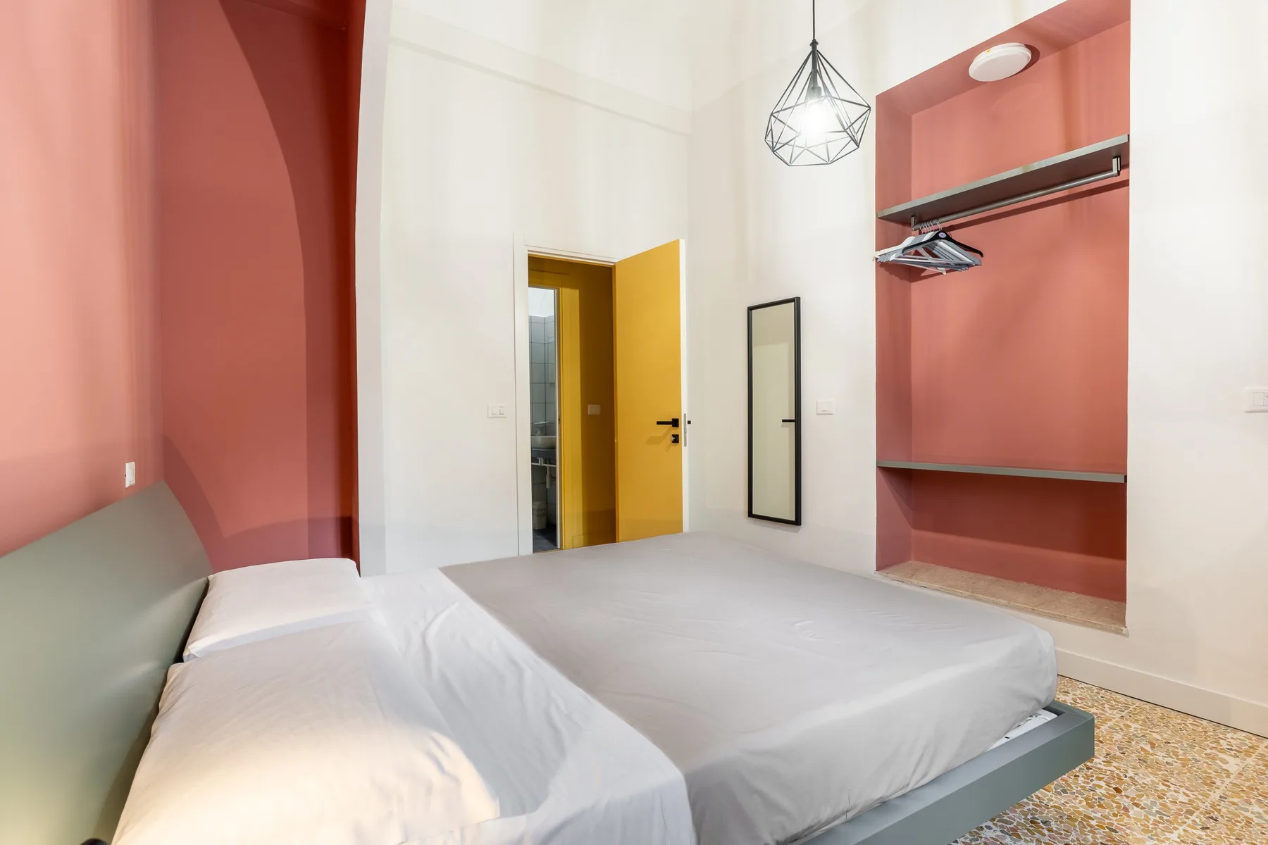 Un dormitorio con una cama, paredes color coral y una puerta amarilla abierta.