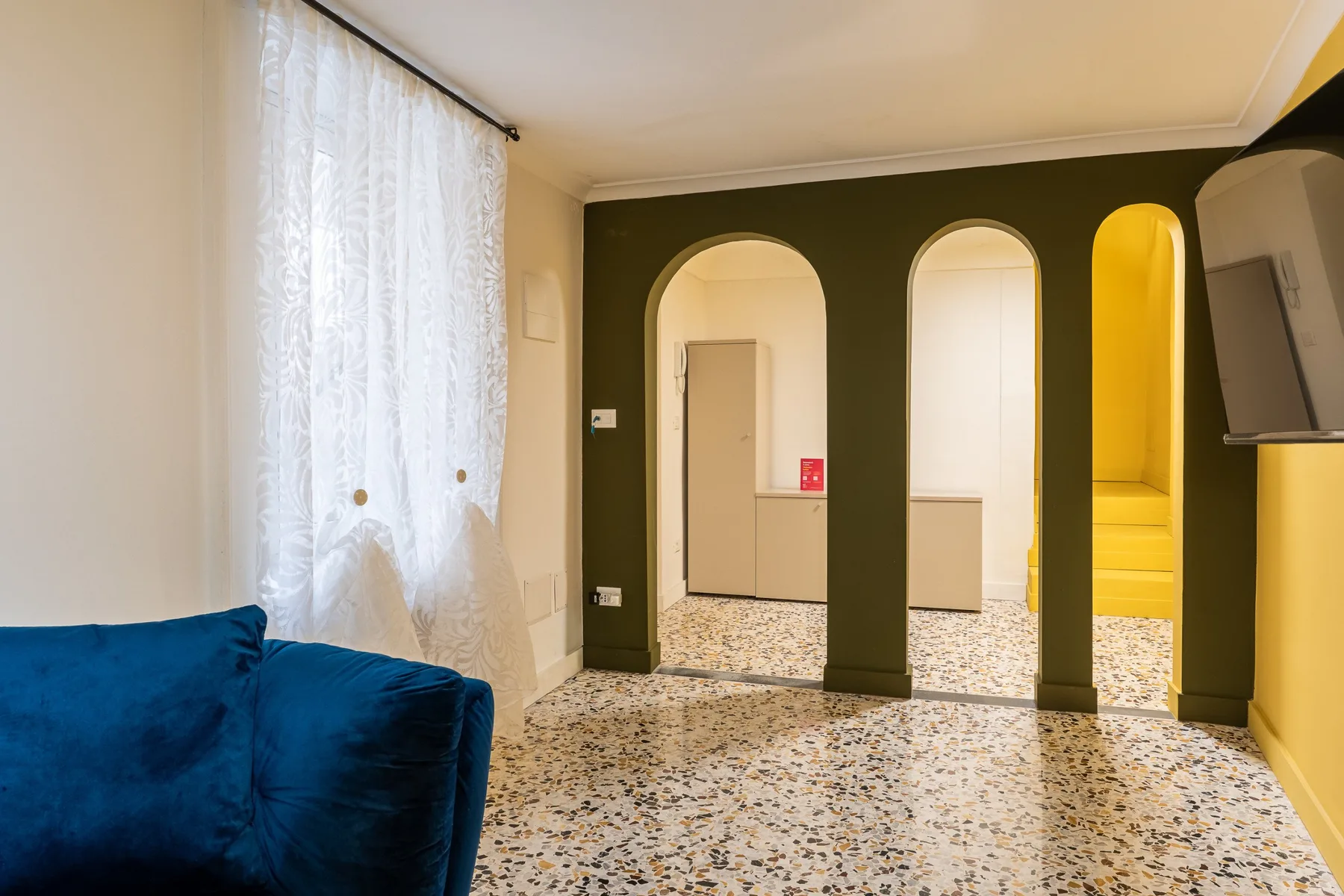 Un pasillo interior con arcos, una zona de asientos azules y suelo de terrazo.