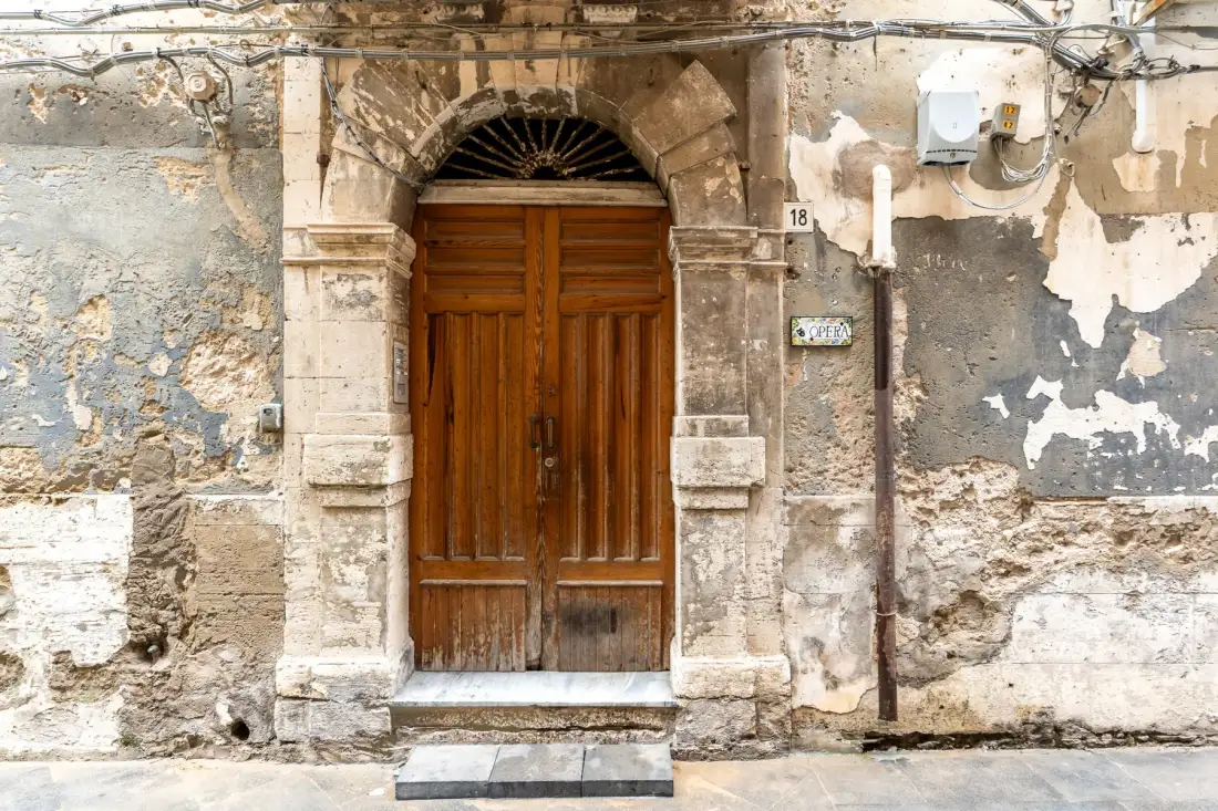 Una antigua puerta de madera en una fachada de piedra desgastada.