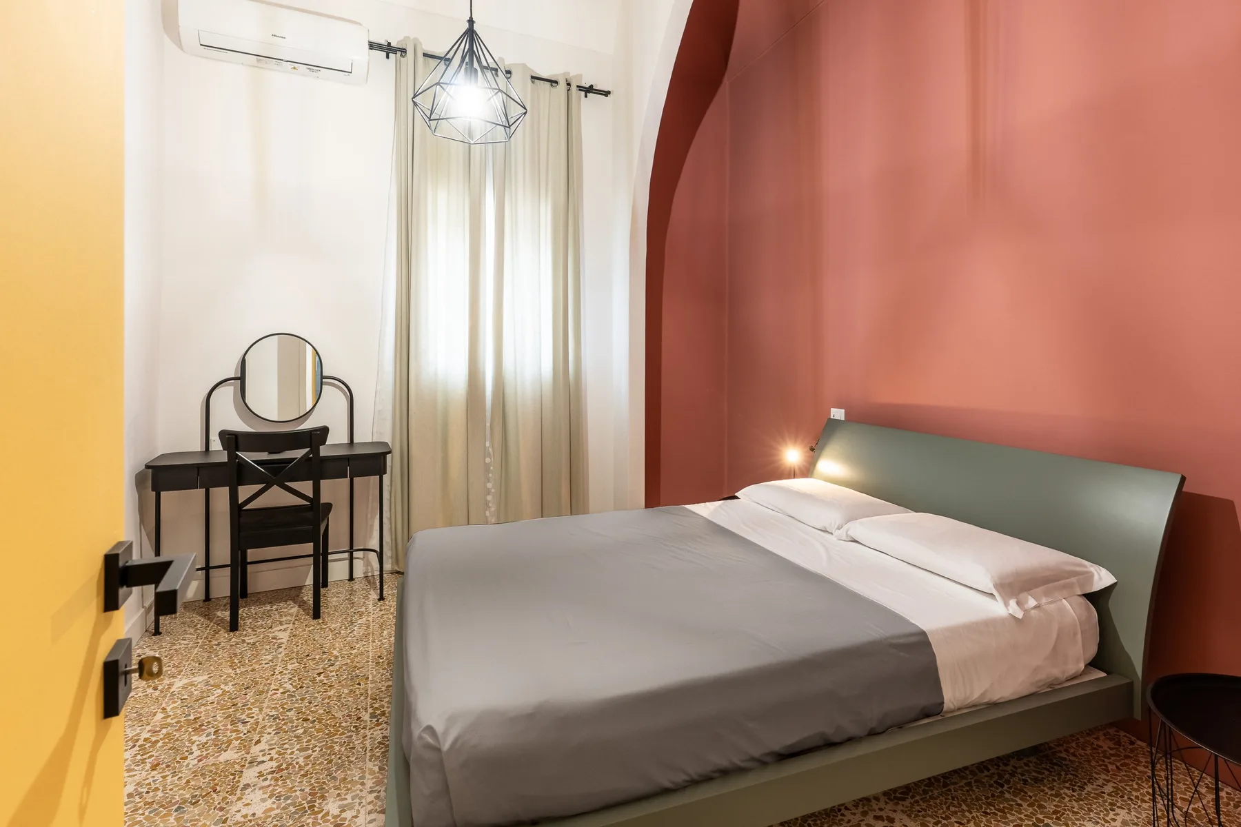 Un dormitorio con una cama bien arreglada y un pequeño tocador junto a la ventana.
