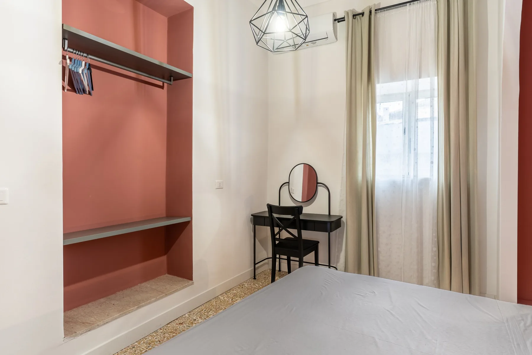 Un dormitorio con un escritorio y un espejo junto a una ventana con cortinas.