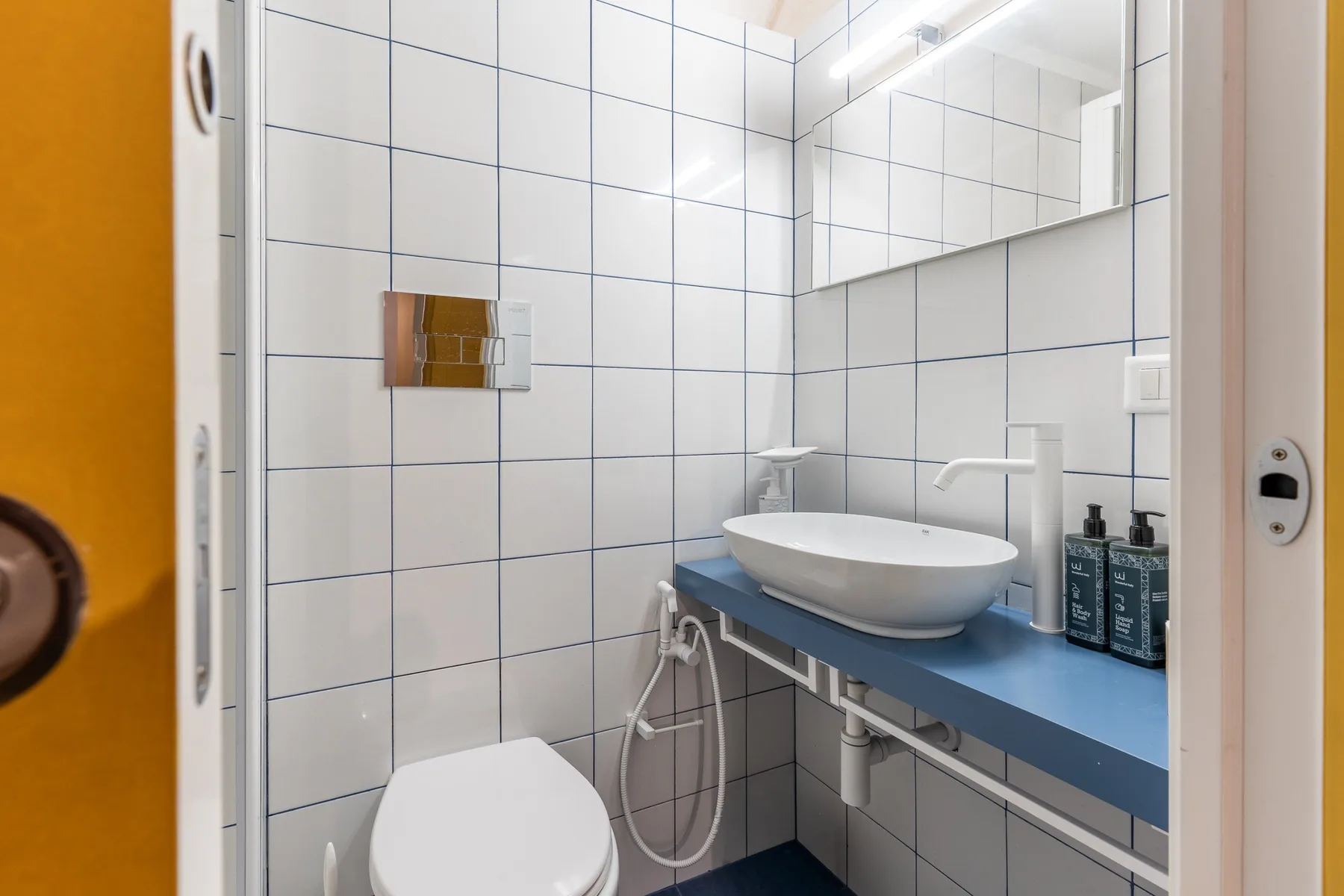 Un baño alicatado con un inodoro y un lavabo sobre una encimera azul.