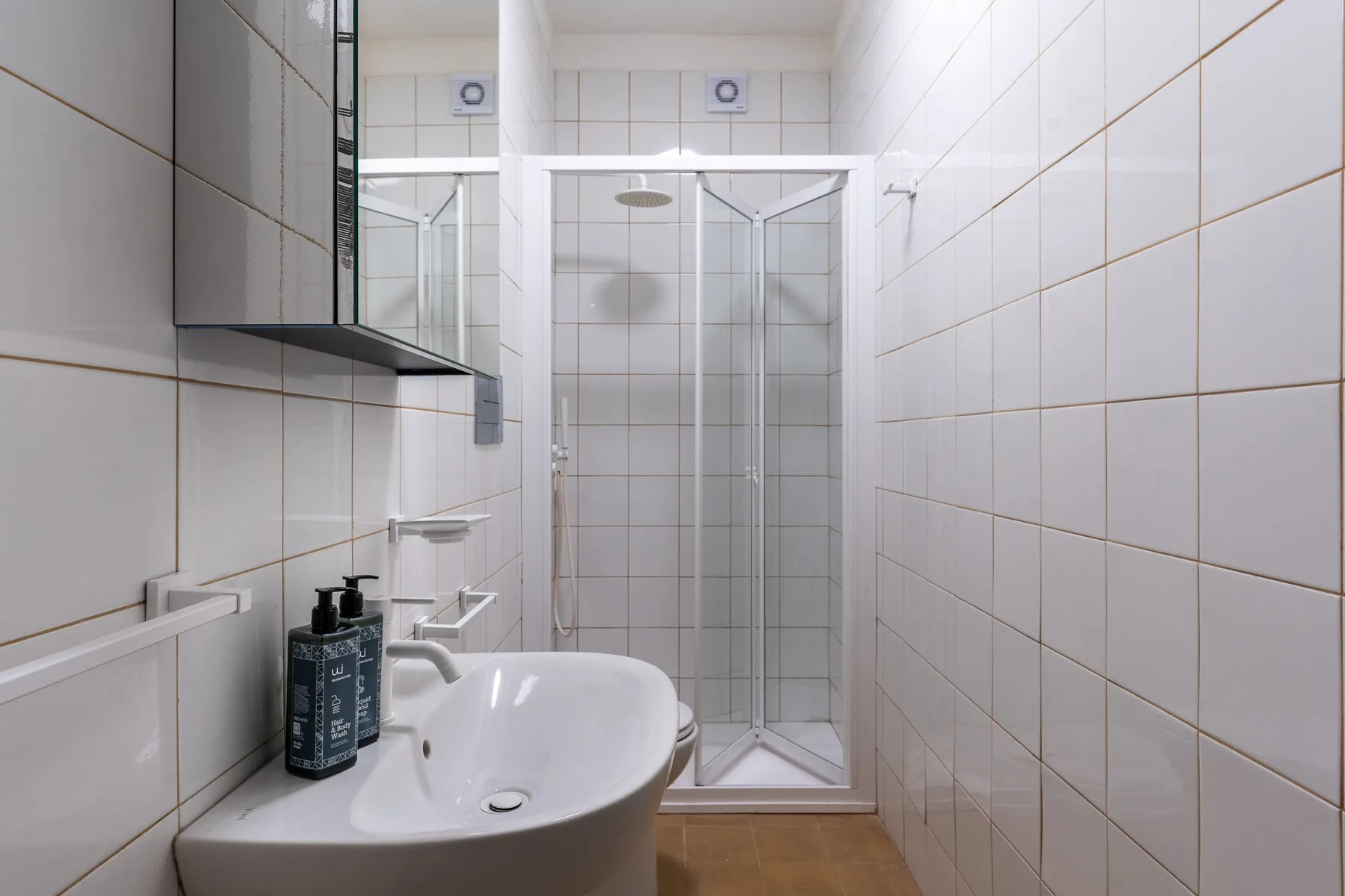 Un baño alicatado con lavabo y ducha de vidrio.