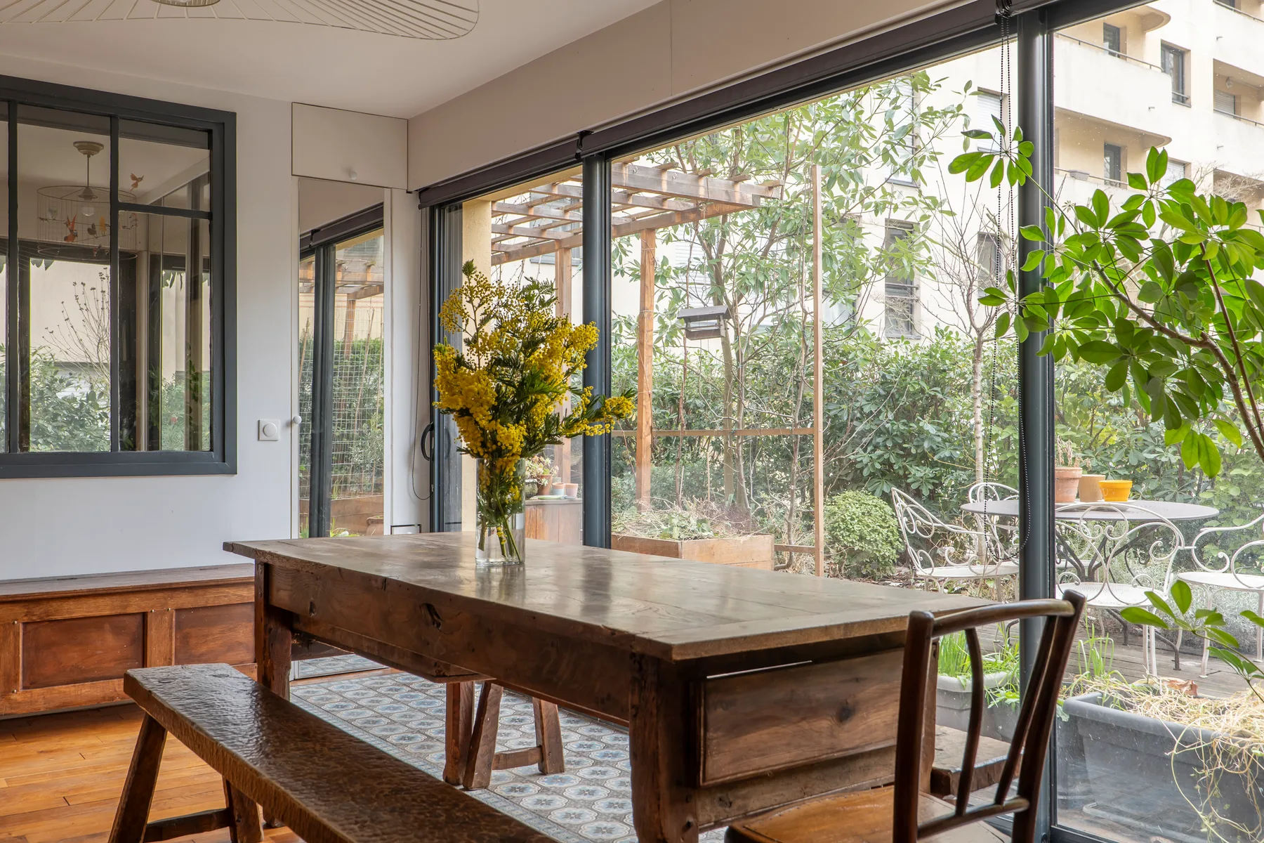 A dining area with a wooden table beside large glass doors opening onto a leafy patio.