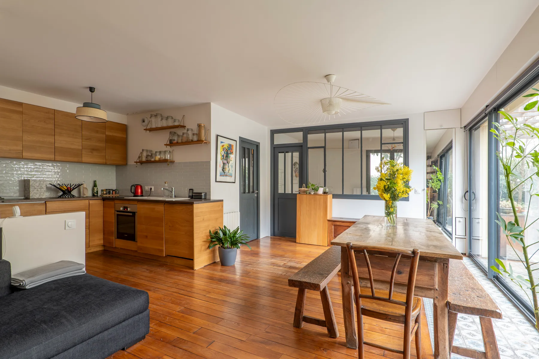 An open-plan kitchen and dining area with a wooden table beside large windows.