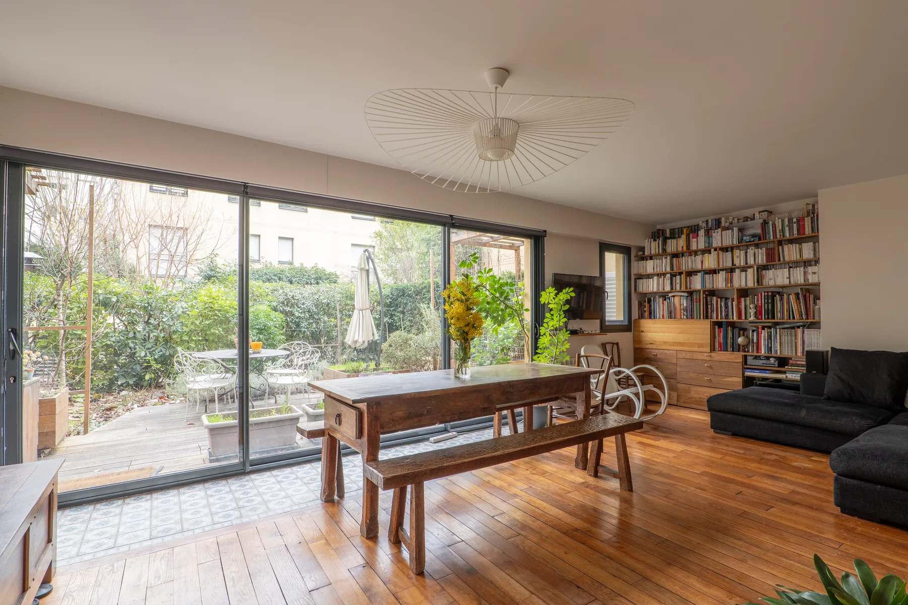 A bright living and dining room with a long wooden table and garden-facing windows.