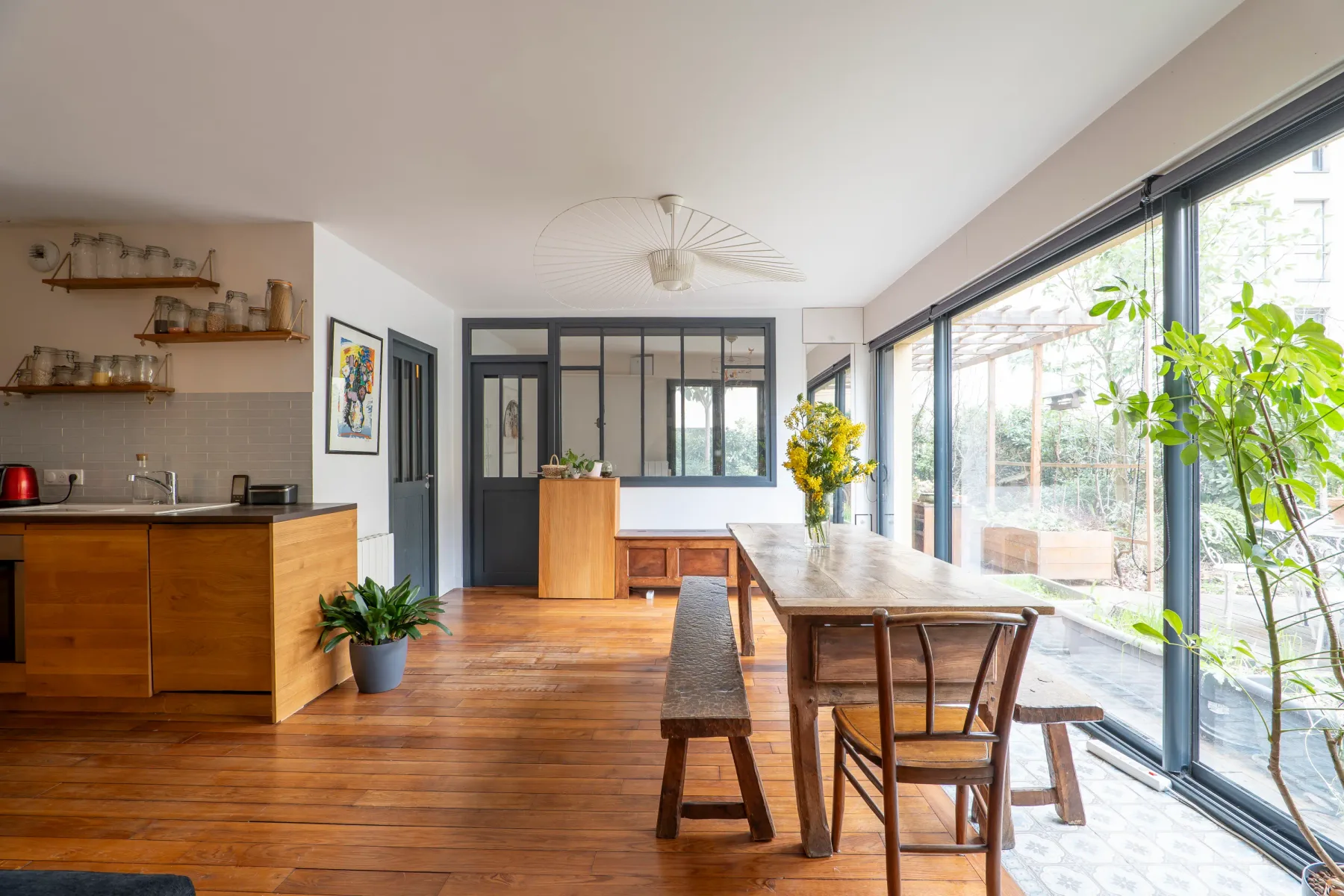 An open-plan kitchen and dining area with a long wooden table beside large windows.